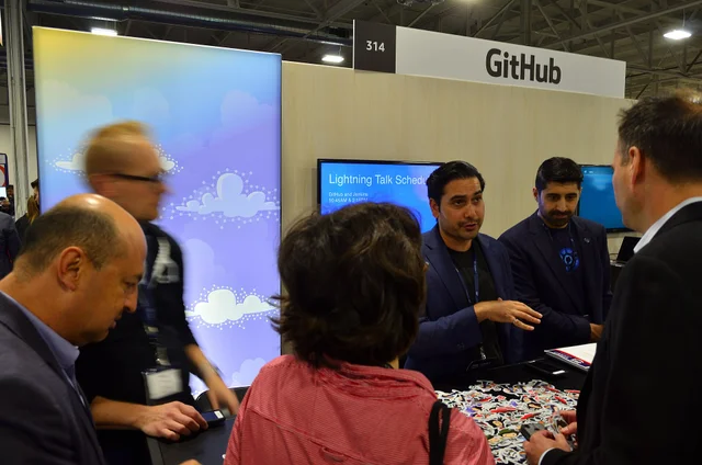 Посетители разговаривают у стенда GitHub на технологической конференции