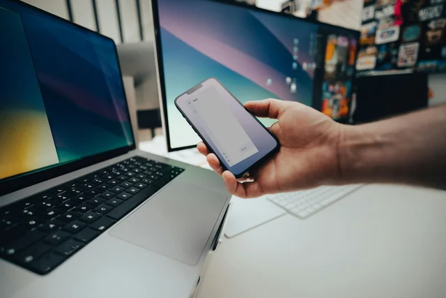 Фотокомпозит: смартфон с интерфейсом Gemini в руке рядом с ноутбуком