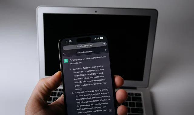 Смартфон с ChatGPT в руке перед ноутбуком